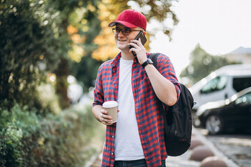 Fototapeta premium Young male student drinking coffee using phone in park