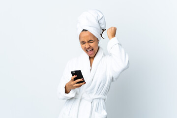 Young woman in bathrobe over isolated white background with phone in victory position
