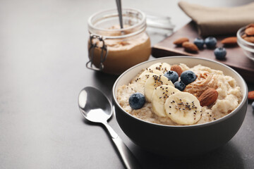 Tasty oatmeal porridge with toppings served on grey table, space for text
