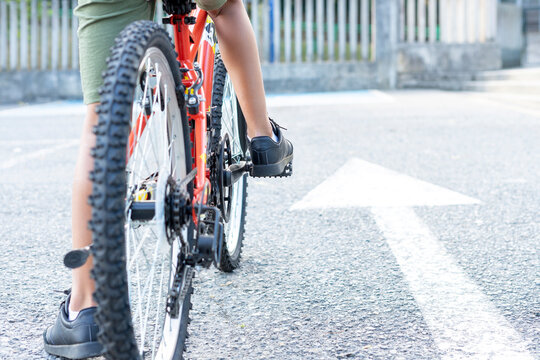 Close up of a child's legs mounted on his bicycle ready to start riding next to a white arrow sign painted on the ground indicating go ahead. Concept Keep going forward. High quality photo