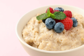 Tasty oatmeal porridge with raspberries and blueberries in bowl on light background, closeup