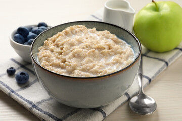 Tasty oatmeal porridge served on light wooden table