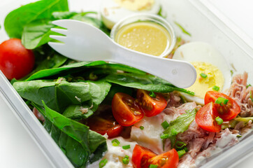 Healthy salad in the plastic food box, potato salad with hard boiled egg, shredded ham, cucumber, tomatoes, lettuce and spinach with a honey and mustard dressing pot