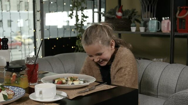 a little girl with blonde hair laughs merrily sitting in a restaurant on a beige sofa. High quality FullHD footage