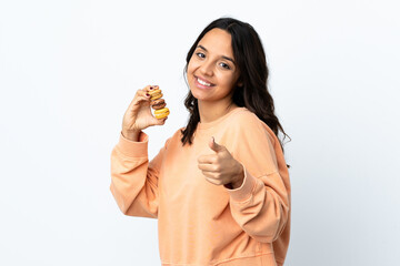 Young woman over isolated white background holding colorful French macarons with thumbs up