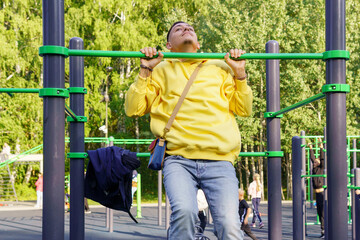 Obraz premium A young man in a yellow jacket pulls himself up on a horizontal bar. Selective focus. Sports event