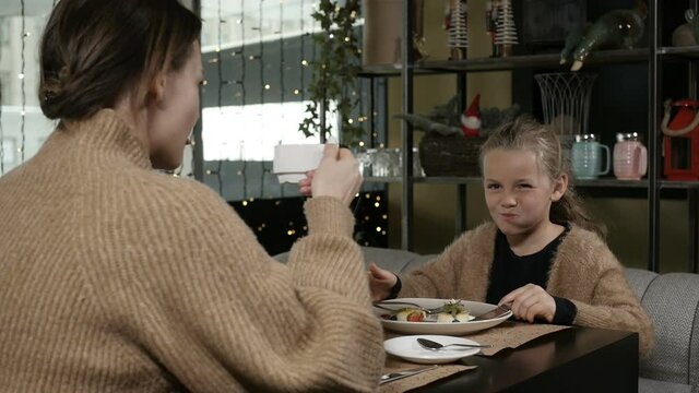 a little girl with long hair eats food sitting in a cafe with her mother. High quality FullHD footage
