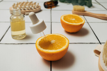Pipette dropper in a freshly cut orange fruit and cosmetic bottle and beauty accessories on a white tile counter top. Natural cosmetics ingredients for skin care. Vitamin eco friendly skincare.