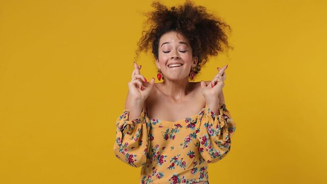 Pleading charming vivid young latin curly woman 20s wears casual flower dress hold hands folded in prayer begging about something making wish keep fingers crossed isolated on plain yellow background