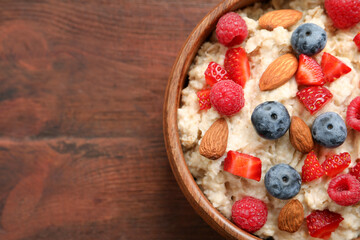Tasty oatmeal porridge with berries and almond nuts in bowl on wooden table, top view. Space for text