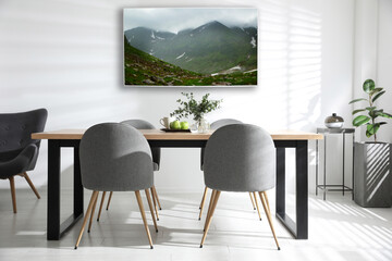 Modern wide screen TV on white wall in room with stylish furniture