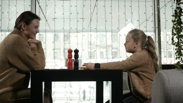 mother and daughter sit together in a restaurant and wait for their order, have fun talking. The concept of family and relationships. High quality FullHD footage