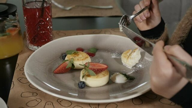 the girls hands cut cheesecakes with berries lying on a white plate. Video to advertise a cafe or restaurant. High quality FullHD footage