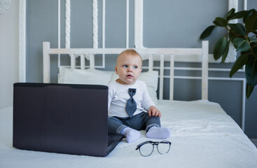 a little boy in a suit is sitting on a bed with a laptop