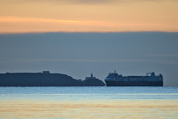 Beautiful early morning view of sea truck ferry ship in Irish Sea near Baily lighthouse seen from Blackrock Beach, Dublin, Ireland. Soft and selective focus. Sunrise marine themed