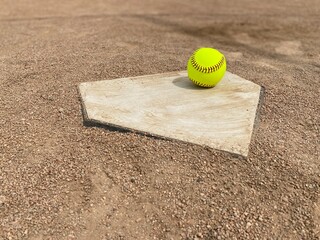 Yellow softball at home plate on a dirt infield