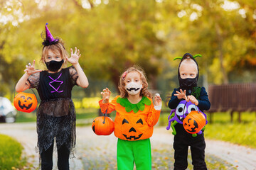 Three kid with a basket for sweets making grimaces wearing face mask on Halloween holiday