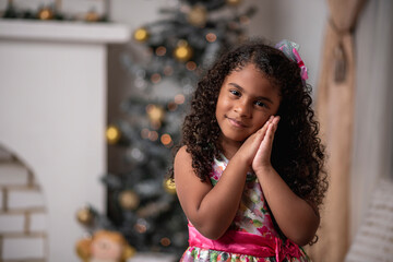 Hermosa niña afro caribeña disfrutando de la navidad con un árbol, adornos y regalos de fin de...