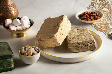 Sunflower and peanut halva is lying on a plate next to a cup with sugar, marshmallows, peanuts. Oriental sweets for tea drinking..