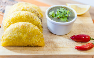 fried empanadas served on a board accompanied by chili pepper, aji and lime.