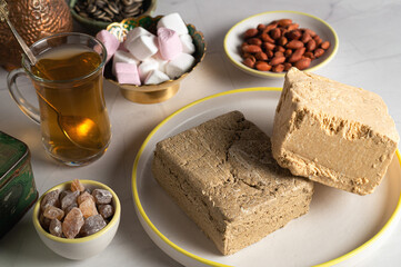 Sunflower and peanut halva is on a plate, next to a cup of sugar, marshmallow air candies, peanuts and a cup of tea. Oriental sweets for a tea party close-up.