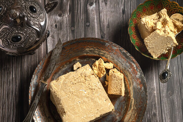 Peanut halva, cut into pieces, lies on a vintage plate with a knife on a dark background. Traditional oriental sweetness for tea drinking. Top view..
