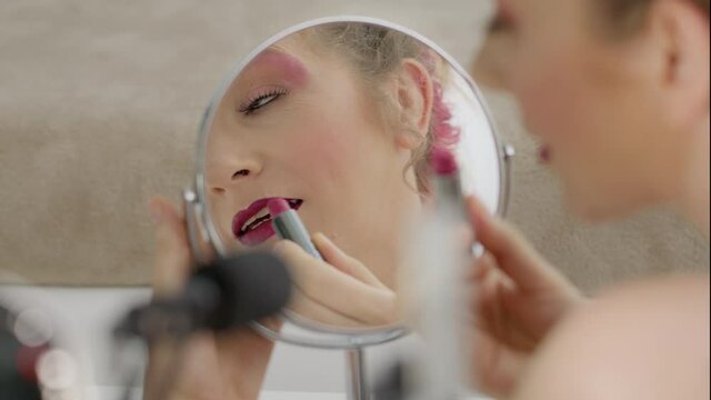 Smiling blonde influencer blogger recording video tutorial, shot close up in the mirror, shows how to apply lip makeup cosmetics. Female vlogger making a beauty vlog for her online internet channel.