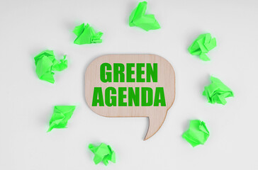 On a white background, there are crumpled green pieces of paper and a wooden sign with the inscription - Green agenda