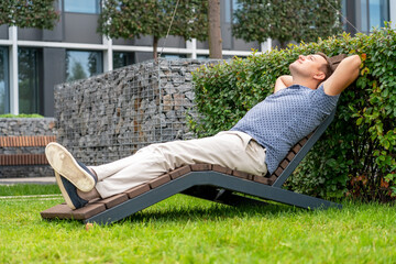 Handsome man relaxing on wooden chaise lounge in city park. Life-work balance and lifestyle concept...