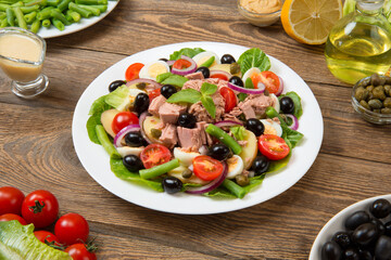 
Traditional Nicoise salad in a white plate on an old rural table with sauce and ingredients. Selected focus. 

