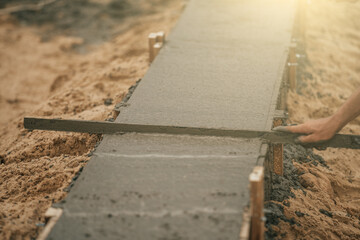 Worker leveling newly poured cement into formwork with reinforcement, building foundation of residential building.