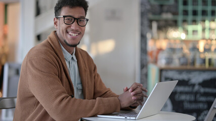 African Man with Laptop Smiling at Camera in Cafe 