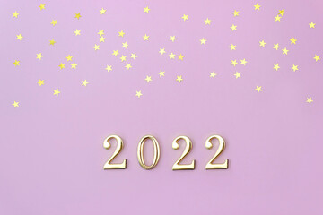 Number 2022 on pink background decorated with golden star confetti. New Year celebration concept