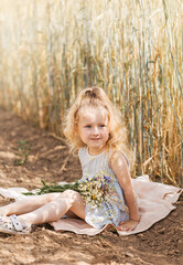 Little cute blonde girl with a bouquet of wildflowers in nature in the summer