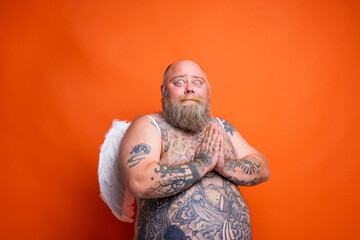 Fat afraid man with beard ,tattoos and wings acts like an angel