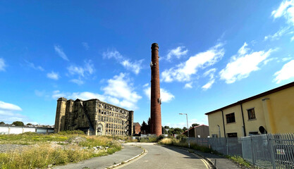 Tall Victorian red brick chimney, next to an old derelict mill, in post industrial  Bradford, Yorkshire, UK