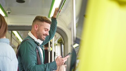 Young caucasian good looking happy man with big headphones on his neck watching something on the smartphone device and laughing in the tram