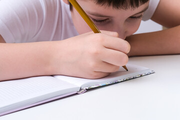 A caucasian boy doing his homework at home, he is focused, concentrated while writing in a notebook