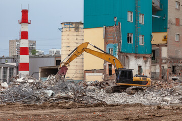 Yellow excavator clears debris after demolition of an old building