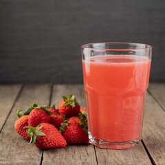 Strawberry juice in a glass with fruits over wooden table