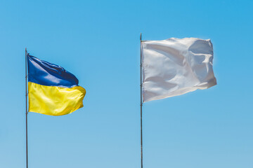 National flag of Ukraine, a symbol of patriotism and the nation of Ukraine against the blue sky opposite the white flag sign and symbol of goodness and truce
