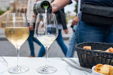 Waiter pouring of brut champagne sparkling wine into glasses in street cafe in old central part of city Reims, Champagne, France