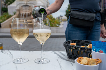 Waiter pouring of brut champagne sparkling wine into glasses in street cafe in old central part of city Reims, Champagne, France