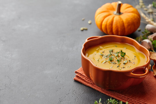 Pumpkin soup with thyme and pumpkin seeds on black background