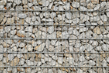 Garden architecture. A wall made of gabions, next to it a bench and a garbage can.