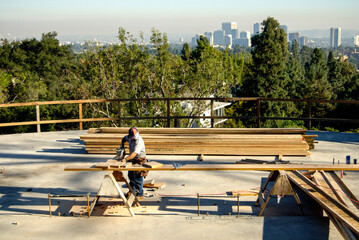 Carpenter sawing long wood studs on a hillside construction project