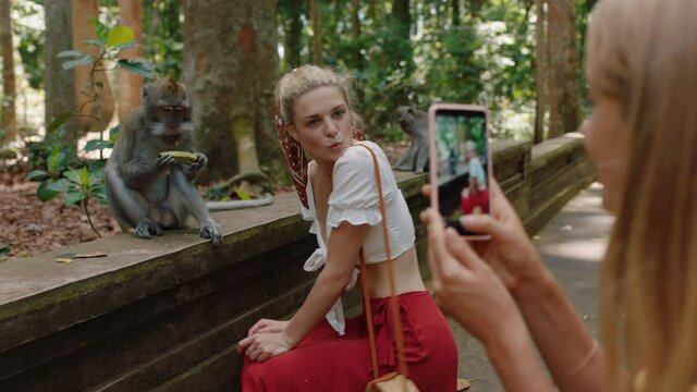 tourist woman using smartphone taking photo of friend posing with monkey in wildlife zoo having fun sharing travel adventure 