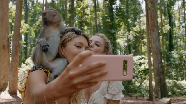 two women using smartphone taking photo of monkey sitting on shoulder girl friends having fun posing with monkeys at wildlife zoo tourists travel bali 