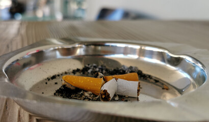 Portacenere in metallo lucido con sigaretta spezzata sul tavolino in legno marrone di un bar