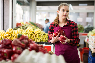 Portrait of a young saleswoman near the counter in a store, laying out bell pepper